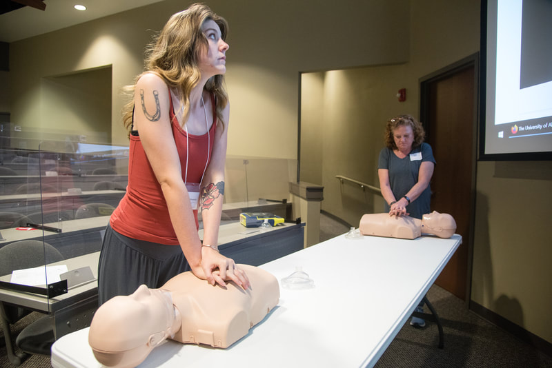 MiMP trainee practices CPR on mannequin, looking up at a video of instructions